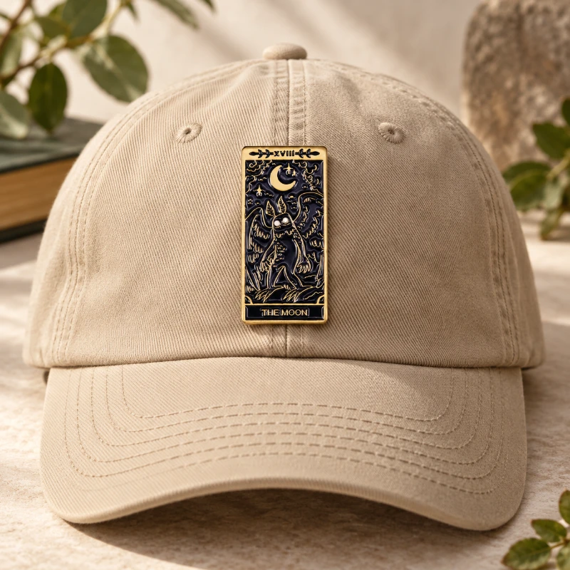 Editorial styling concept of a moon-and-moth pin on a sand-colored cap.